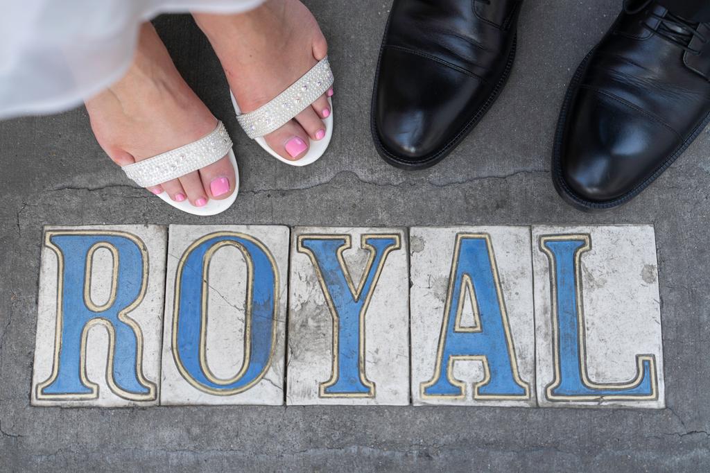 Bride and groom's feet stand over "ROYAL" street tiles in New Orleans, bright light
